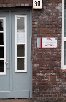 Die graue Eingangstür der Beratungsstelle. Auf der roten Klinkerwand neben der Tür ist ein Schild mit dem Zornrot-Logo zu sehen. Oberhalb der Tür steht die Hausnummer 38.