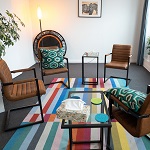 Ein Raum mit vier Stühlen aus braunem Kunstleder und einem bunten Teppich.